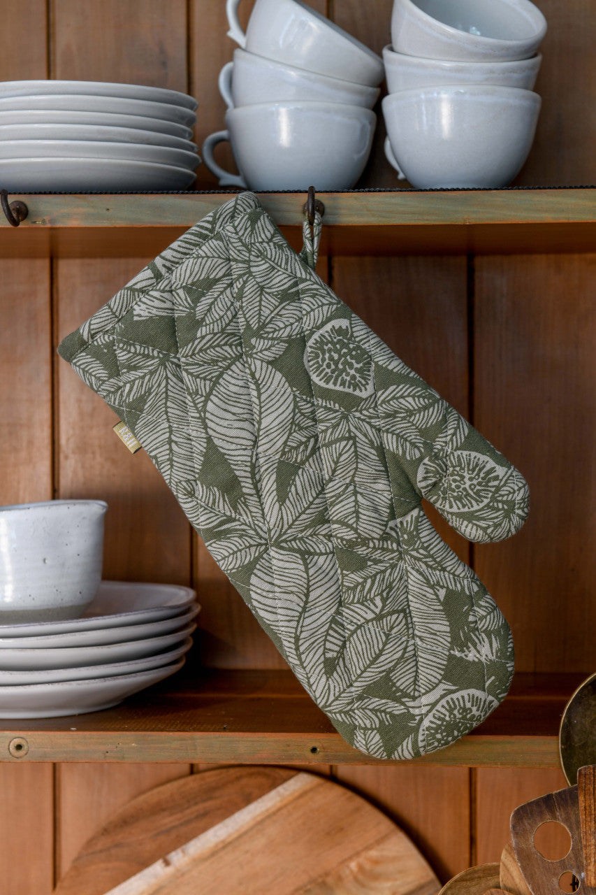 olive green oven mitt hanging on a wooden cabinet filled with white dishes.