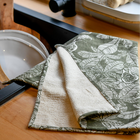 olive green dishtowel with cream terry backing draped on a kitchen counter next to the sink.