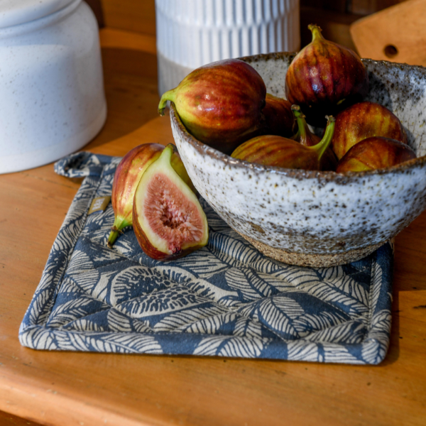 blue and natural pot holder with fig and leaf pattern on a table with a bowl of figs set on it.