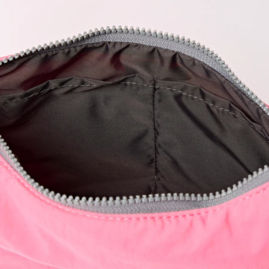interior view of pink shoulder bag with crescent shape and light grey strap shown on a white background
