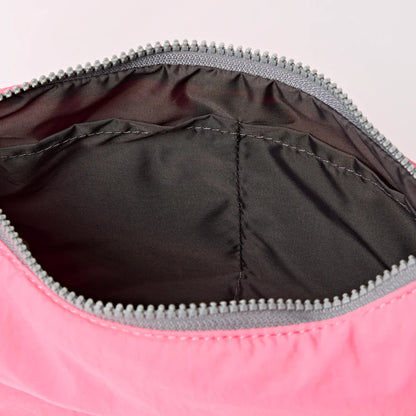 interior view of pink shoulder bag with crescent shape and light grey strap shown on a white background