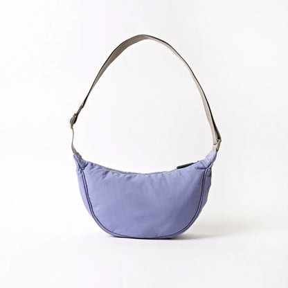 back view of lavender shoulder bag with crescent shape and grey strap shown on a white background