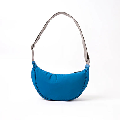 back view of bright Blue crescent shaped shoulder bag with a gray strap on a white background