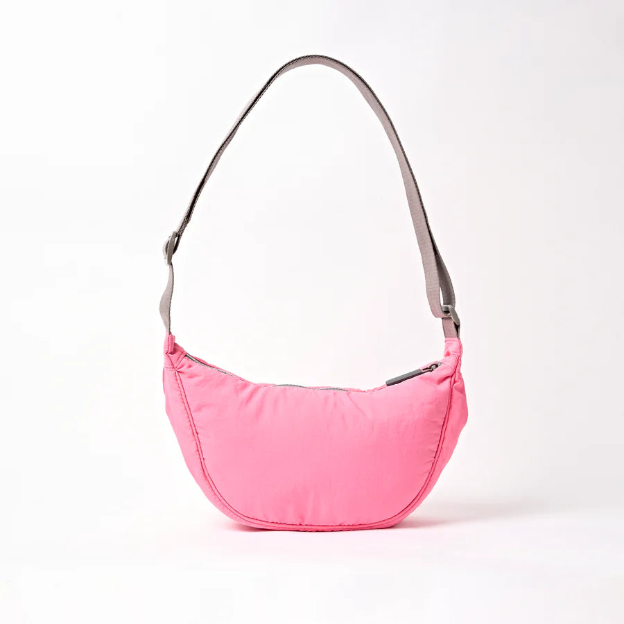back view of pink shoulder bag with crescent shape and light grey strap shown on a white background
