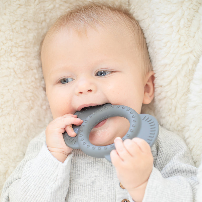 baby laying down chewing on elephant teether.