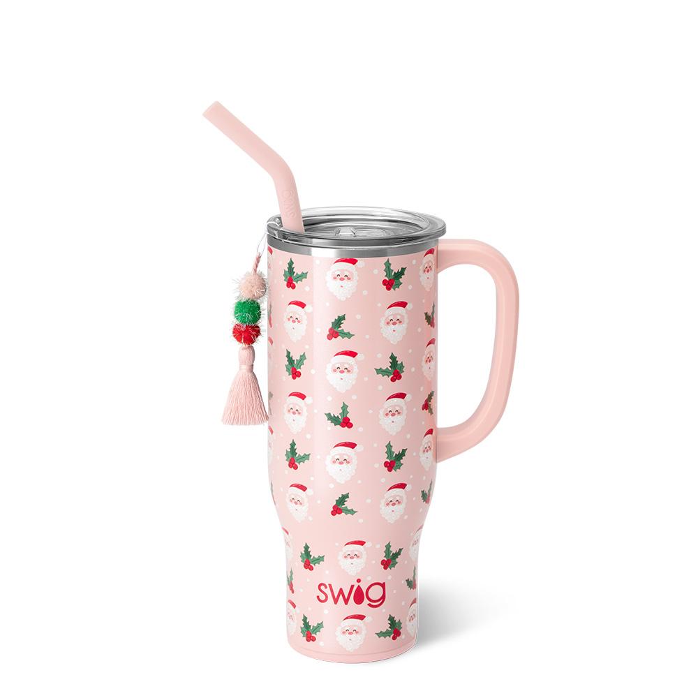 pink tumbler with all-over pattern of Santa faces and sprigs of holly, the tumbler has a pink tassel hanging on it.