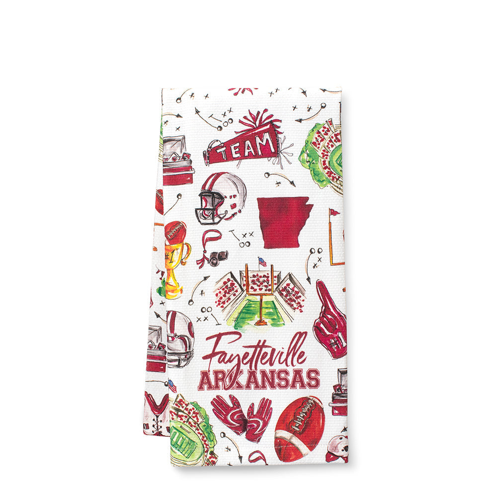 A folded white tea towel featuring a colorful Arkansas Razorbacks football theme print with illustrations of helmets, trophies, a football, and the text 'Fayetteville ARKANSAS' 