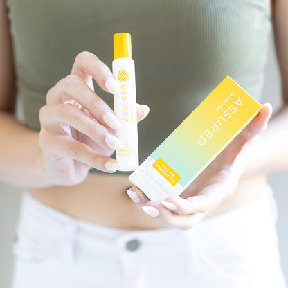 Person holding Assured perfume and its box on a blurred background