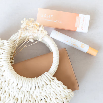 perfume and its packaging arranged on a grey surface with a braided bag and dry botanicals