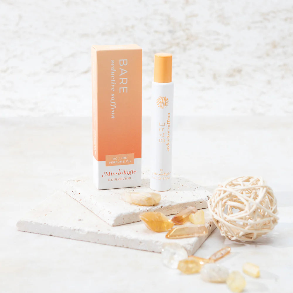 roller perfume bottle with packaging on a textured white surface with seaglass scattered about