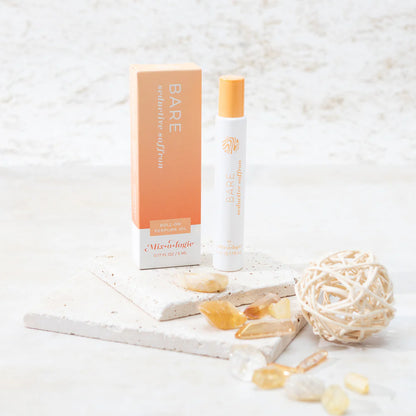 roller perfume bottle with packaging on a textured white surface with seaglass scattered about