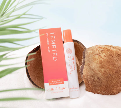 Tempted Coconut Kiss perfume oil with packaging on a white surface with coconuts and green leaves.