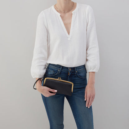 person wearing jeans and a white top holding a black Cora Large Frame Wallet as a clutch.