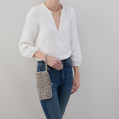 person wearing jeans and a white top holding leopard Cora Large Frame Wallet by the wristlet strap.