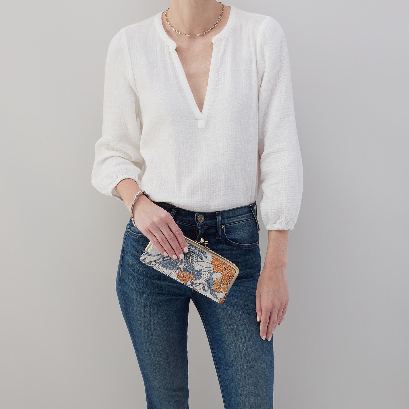 person wearing jeans and a white top holding ornage blossom Cora Large Frame Wallet as a clutch.