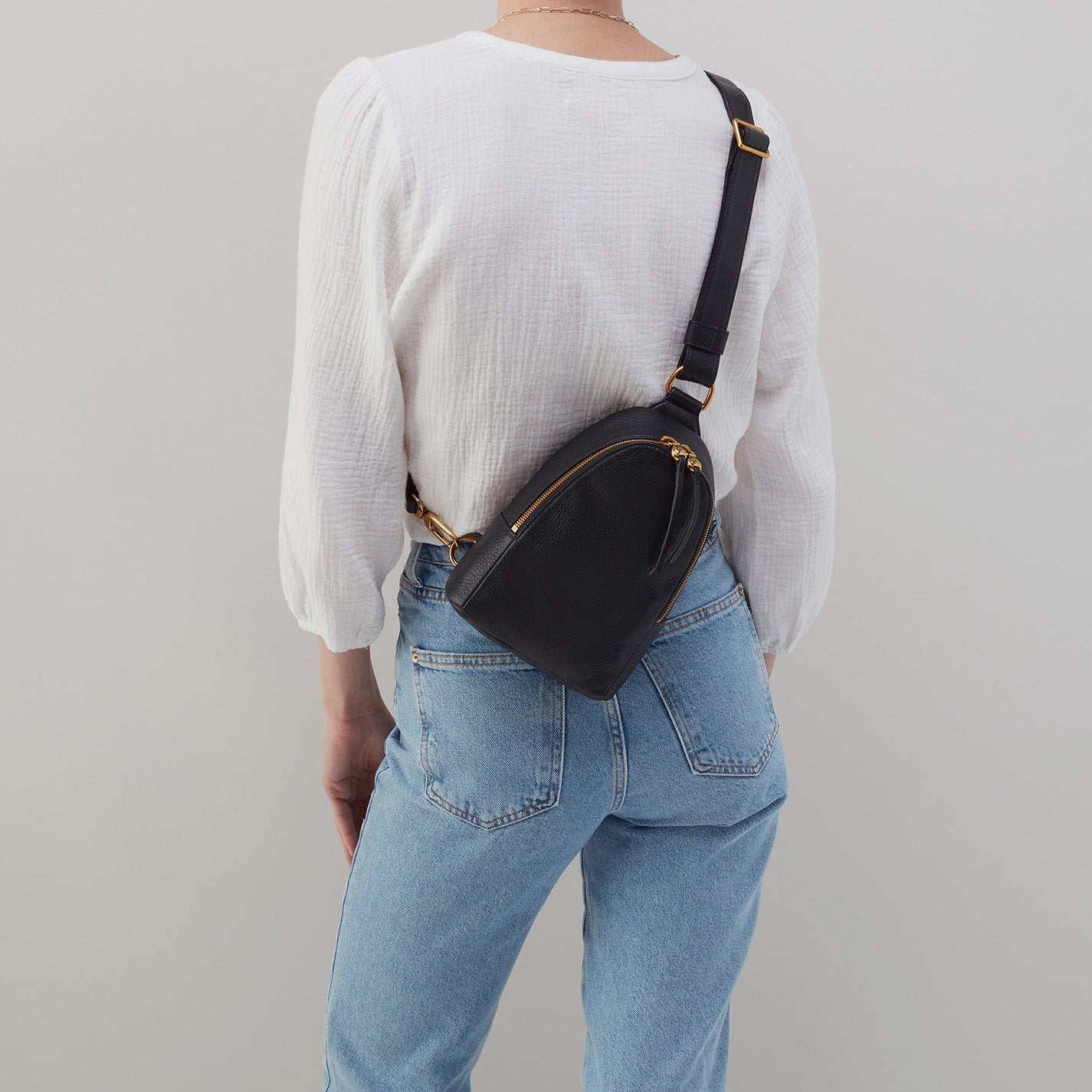 person wearing jeans and a white blouse with black fern sling on their back.