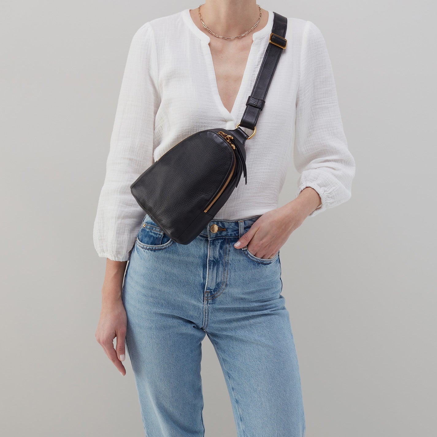 person wearing jeans and a white blouse with black fern sling across their chest.