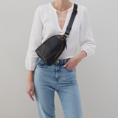 person wearing jeans and a white blouse with black fern sling across their chest.