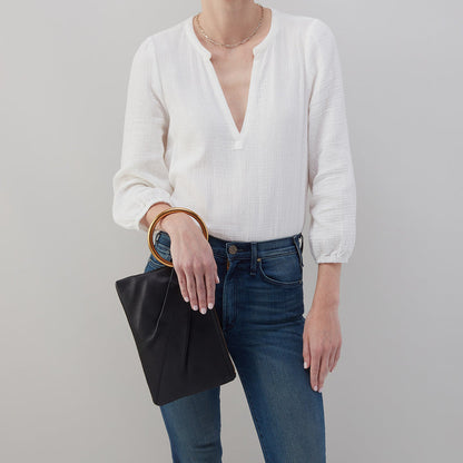 person wearing jeans and a white blouse holding a black ring clutch on their arm.