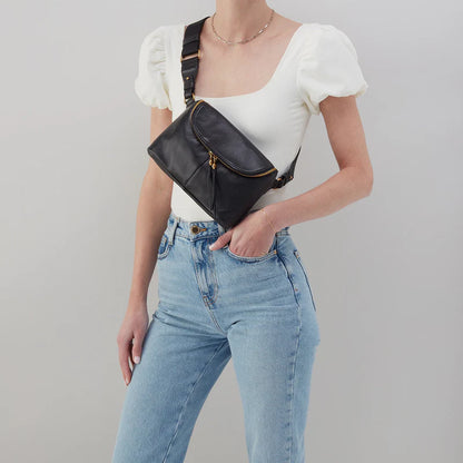 person wearing jeans and a white top with black fern bag across their chest.