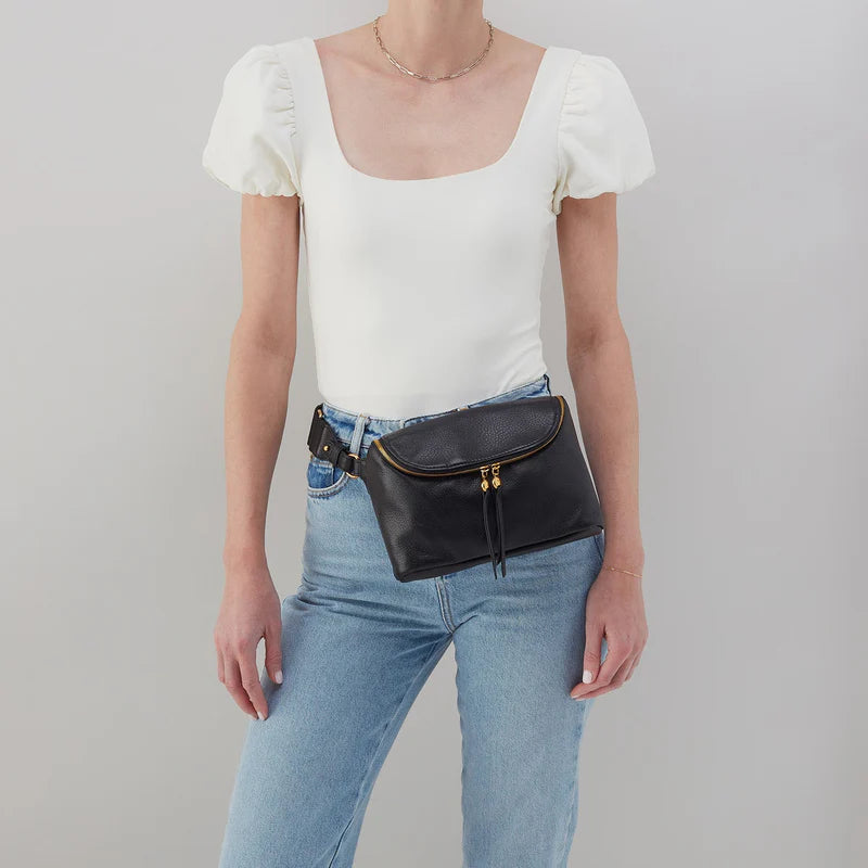 person wearing jeans and a white top with black fern bag around their waist.