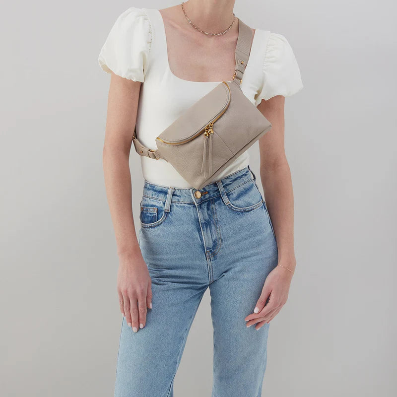 person wearing jeans and a white top with taupe fern bag across their chest.