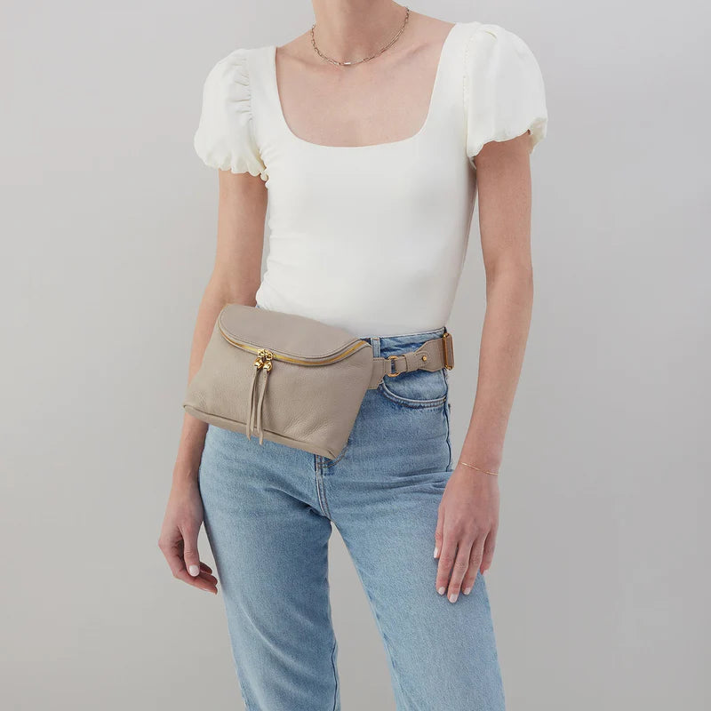 person wearing jeans and a white top with taupe fern bag around their waist.