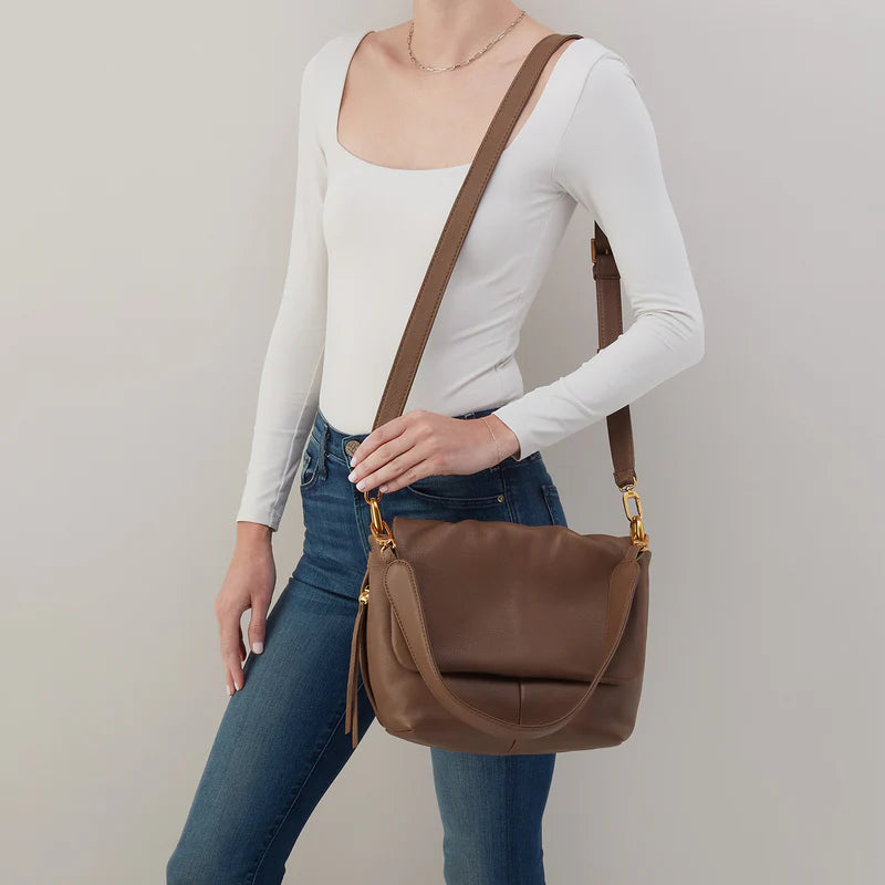 person wearing jeans and a white top with a harley bag on their shoulder.