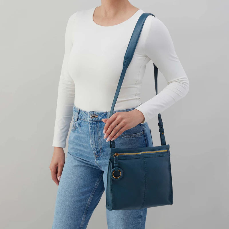 Person wearing jeans and a white top with Peacock Austin medium crossbody on their shoulder