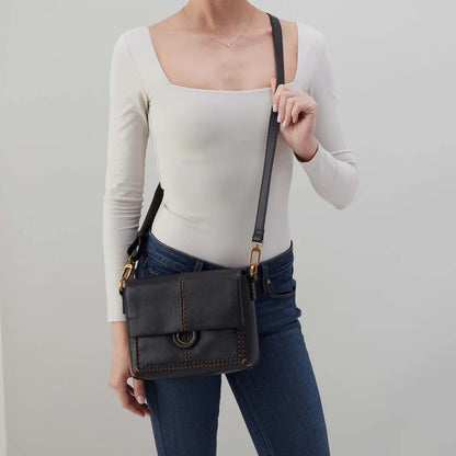 Person wearing jeans and a white top with black Austin flap crossbody over their shoulder