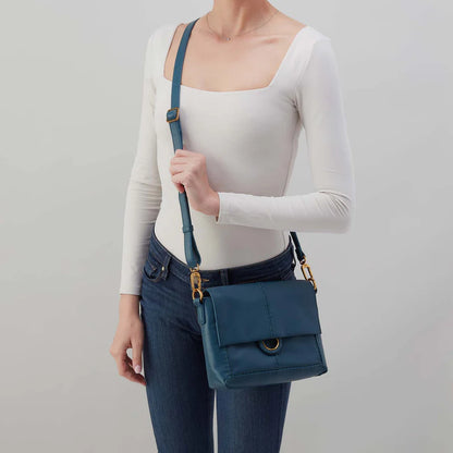 Person wearing jeans and a white top with Peacock feather austin flap crossbody over their shoulder