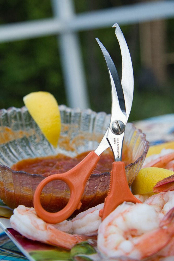sea shrimper scissors propped up on a bowl of cocktail sauce with shrimp around it