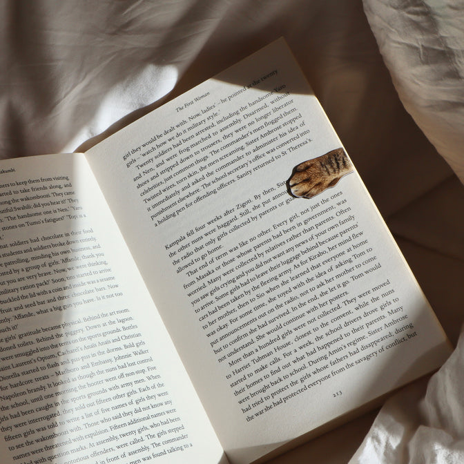 Magnetic Cat Paw Bookmark displayed in a open book on a bed.