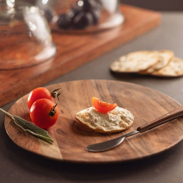 wooden plate with tomatoes, cracker with spread and and small knife set on it.
