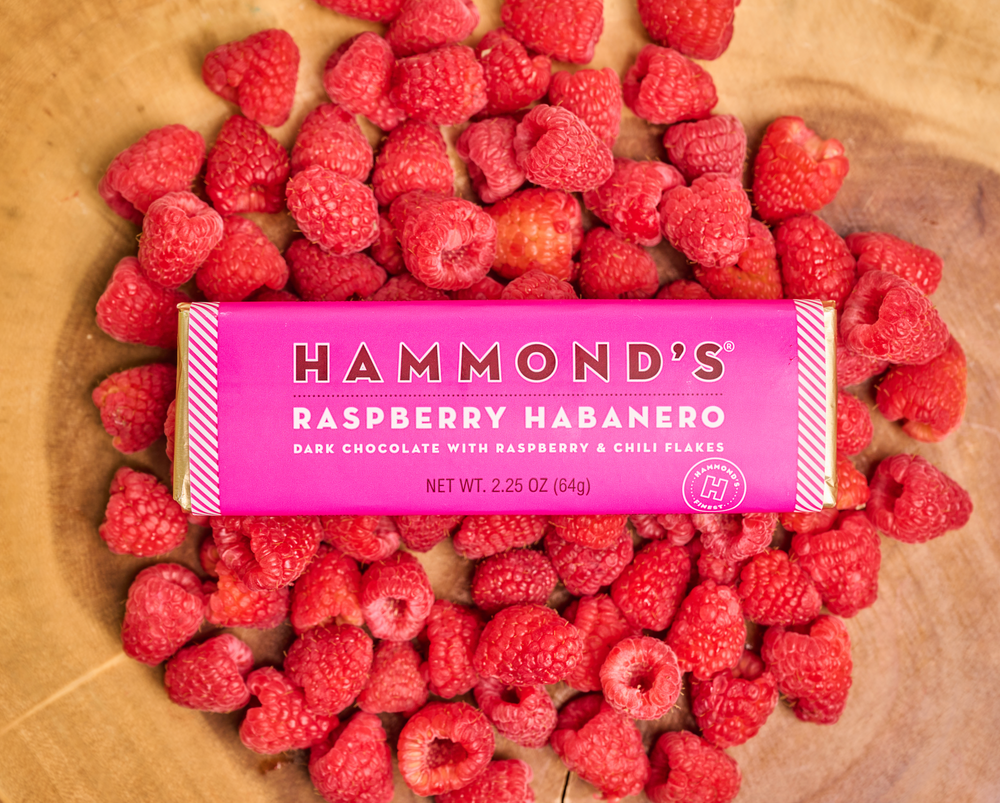 Raspberry Habanero Dark Chocolate Candy Bar laying in a wooden bowl filled with fresh raspberries.