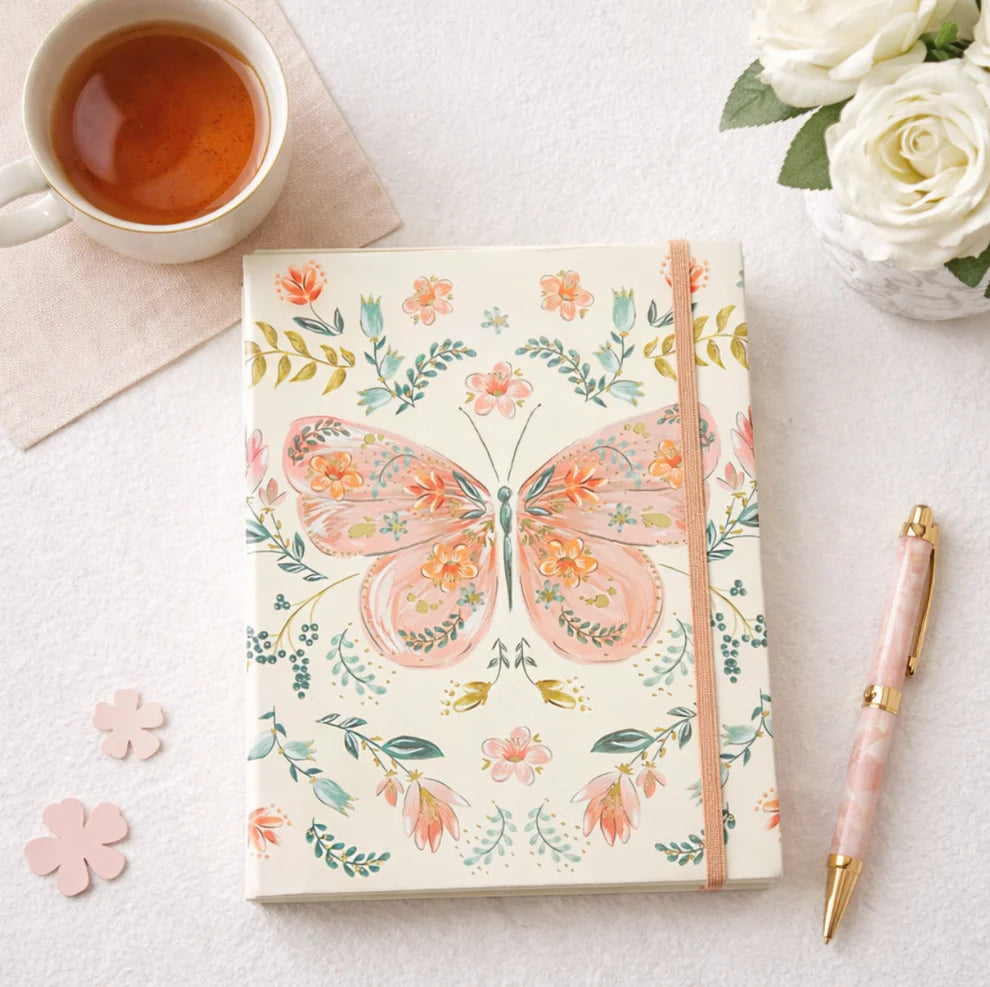 Notebook with butterfly design on a white surface with tea and flowers.