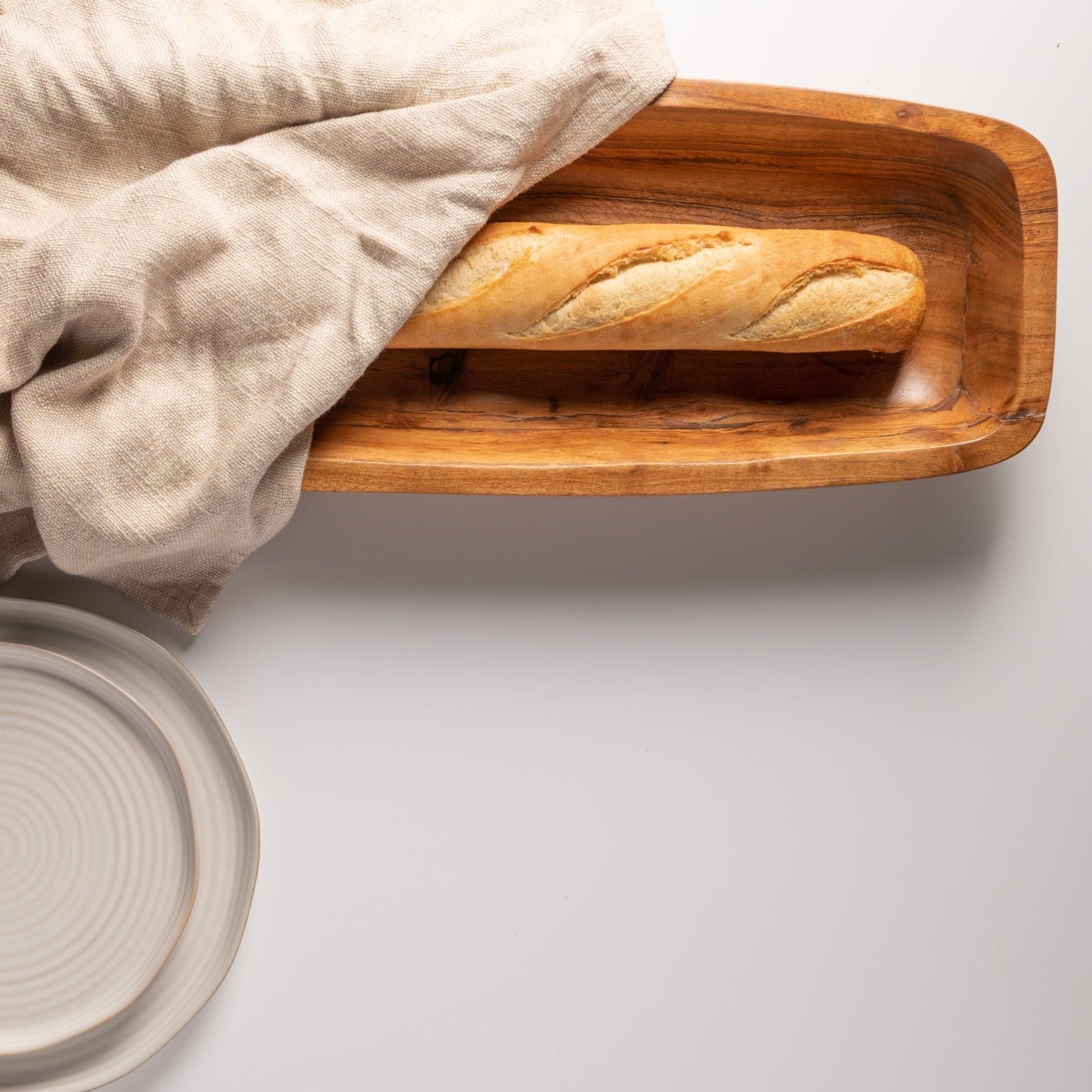 top view of table with wooden bowl filled with loaf of bread wrapped in a towel.