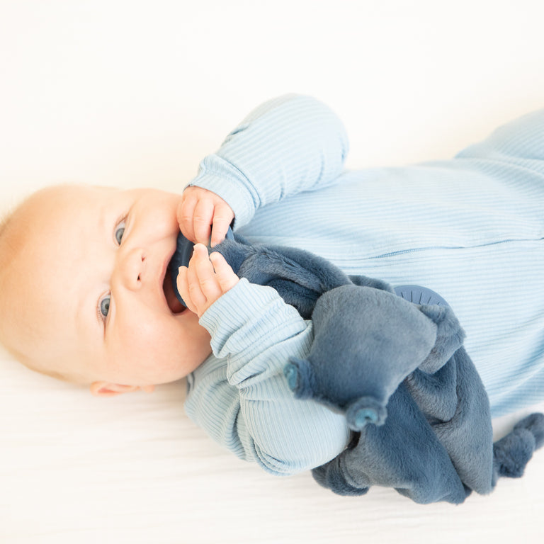 baby laying down chewing on hippo teether.