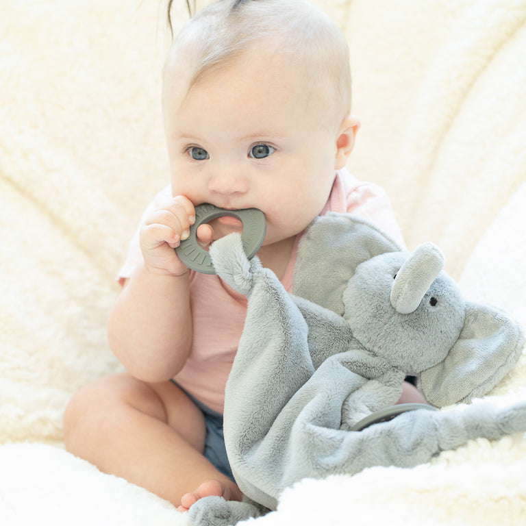 baby sitting up chewing on elephant teether.