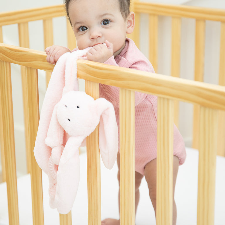 baby standing in crib chewing on bunny teether.
