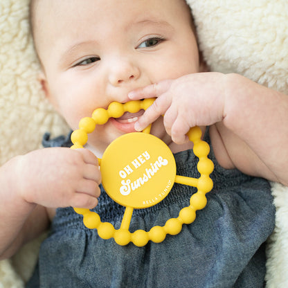 baby laying down and chewing on "oh hey sunshine" teether.