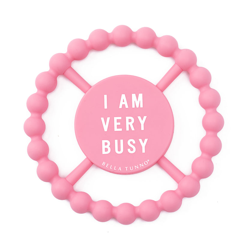 pink silicone teether with "i am vey busy" printed in white in the center.