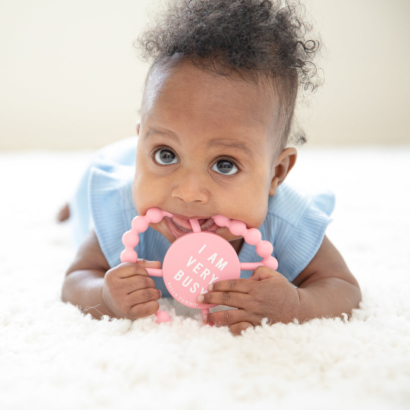 baby laying on their tummy with "busy" teether in their mouth.