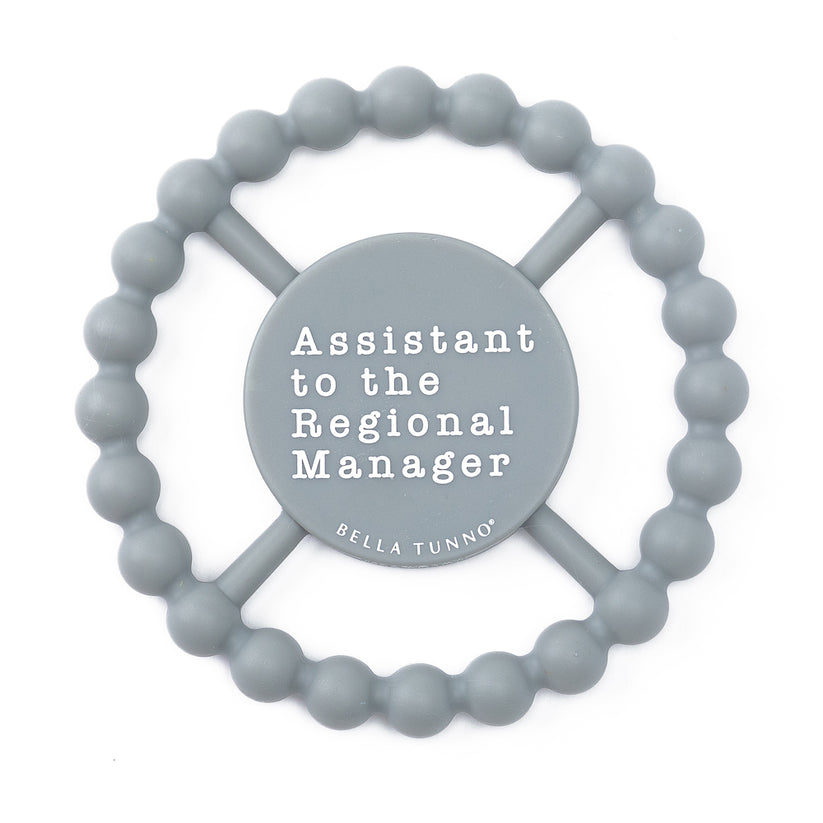 grey silicone teether with "assistant to the region manager" printed in white in the center.