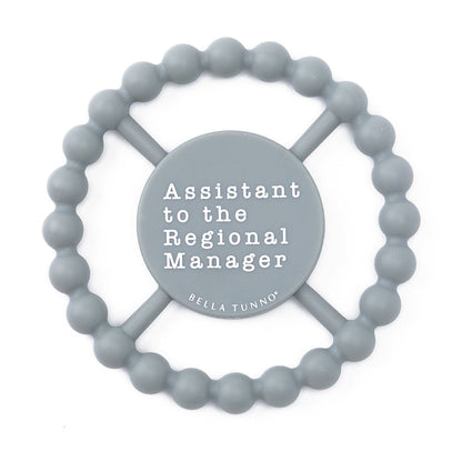 grey silicone teether with "assistant to the region manager" printed in white in the center.