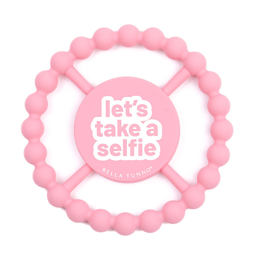 light pink silicone teether with "let's take a selfie" printed in white in the center.