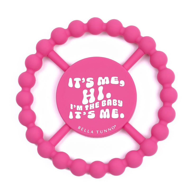 pink silicone teether printed with "it's me, hi. i'm the baby it's me" in white.