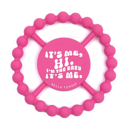 pink silicone teether printed with "it's me, hi. i'm the baby it's me" in white.