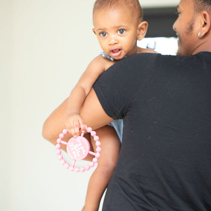 back view of grown-up holding baby who is holding pink "it's me" teether.