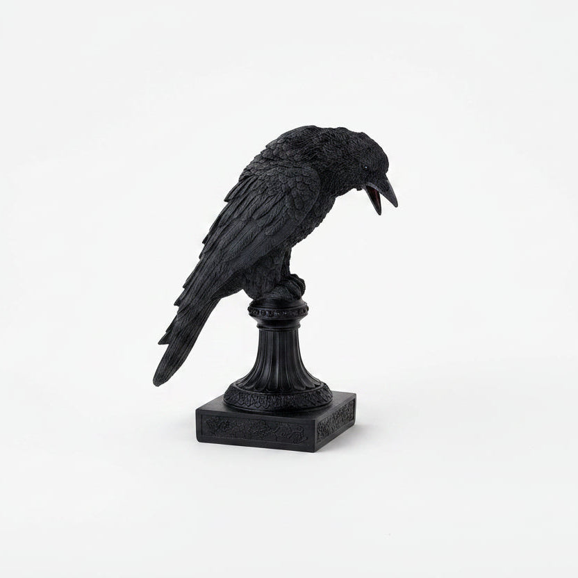 A black crow figurine perched on a decorative pedestal base, shown against a seamless white background.